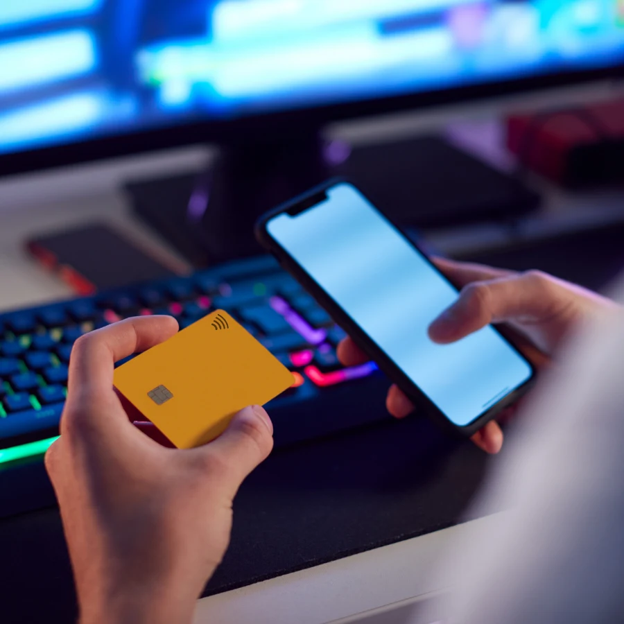 Pessoa segurando um celular e um cartão diante de um computador